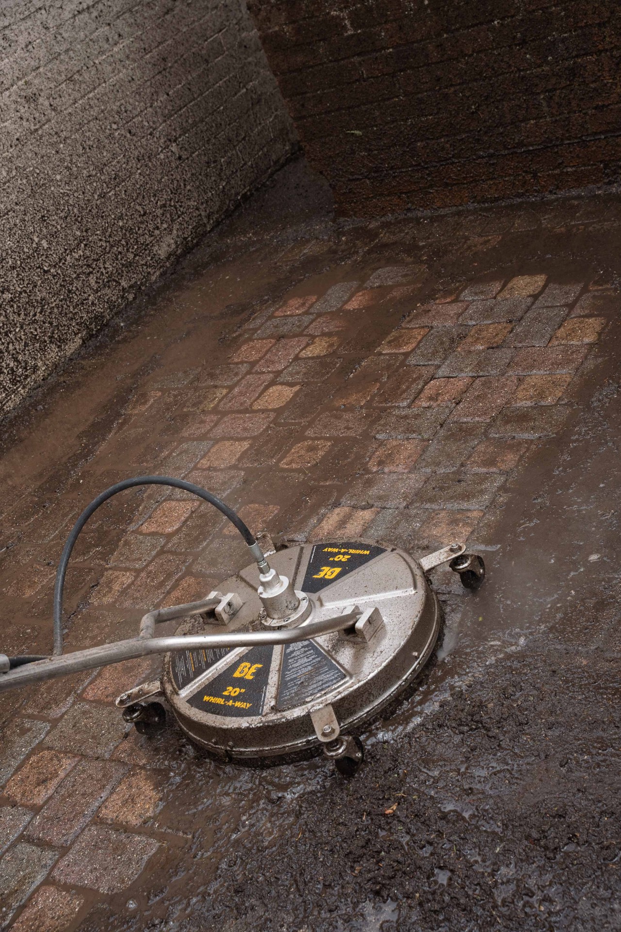 Close-up of a commercial rotary surface-cleaner head over freshly cleaned block paving