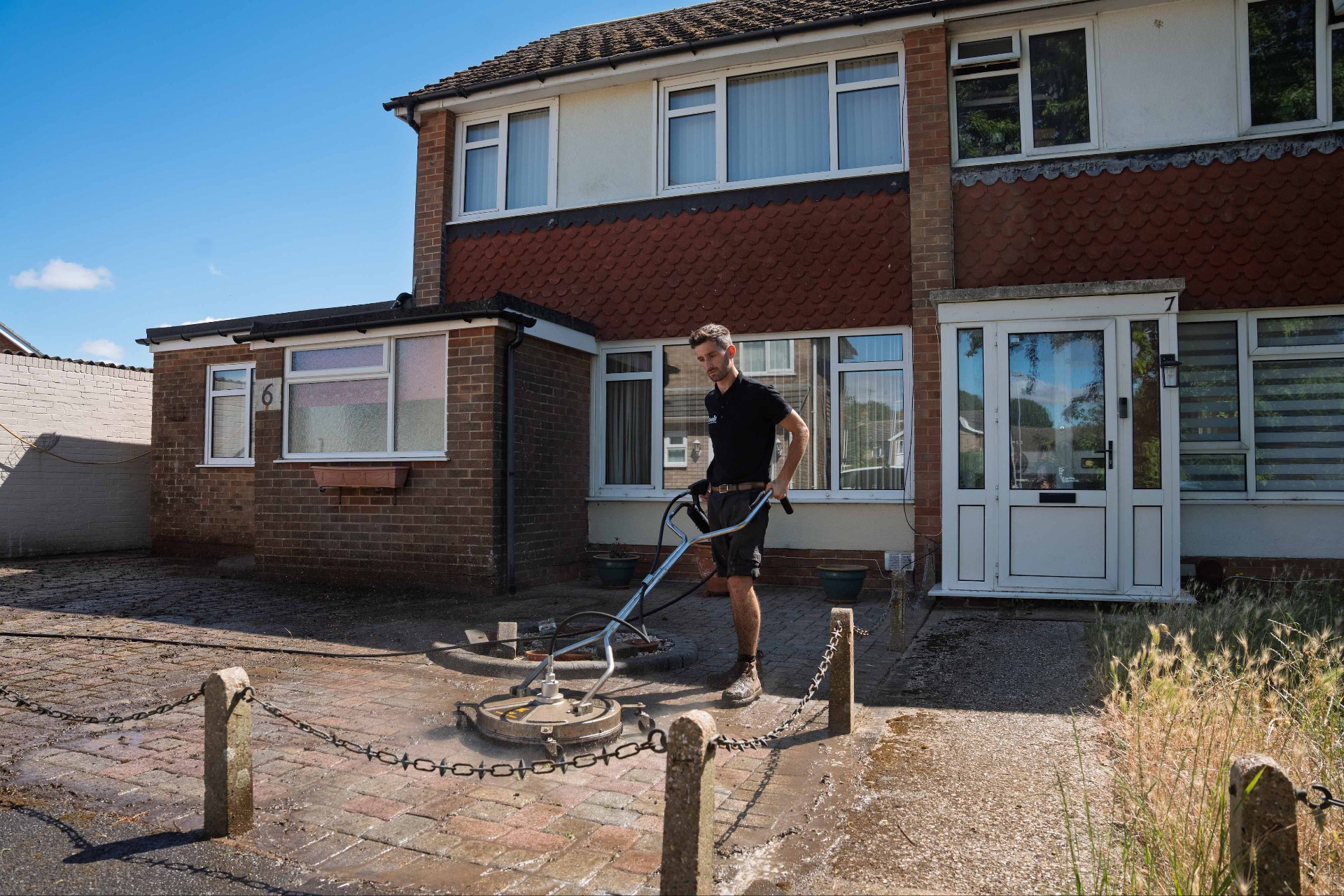 Rinata technician cleaning a block paving driveway with a commercial rotary surface cleaner outside a UK home